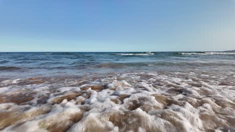 low angle view of waves breaking on sandy beach under a calm, clear blue sky
