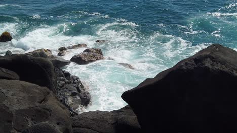 HD-Slow-motion-Hawaii-Kauai-static-looking-down-to-ocean-waves-swirling-and-building-and-crashing-on-rocks-below-with-lava-rocks-in-v-shaped-foreground