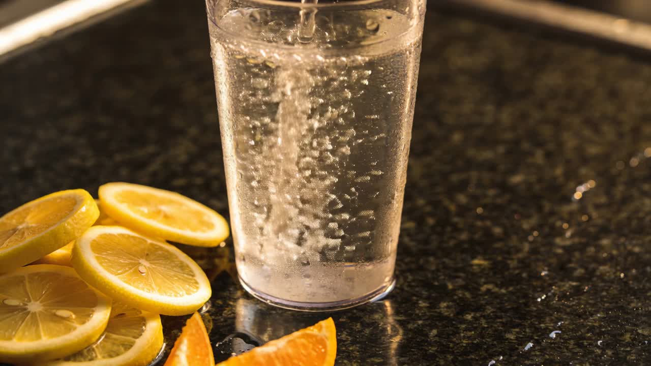 Si versa da una brocca in un bicchiere su un bancone scuro, con bolle che salgono e si attaccano mentre si prepara una bevanda agli agrumi.