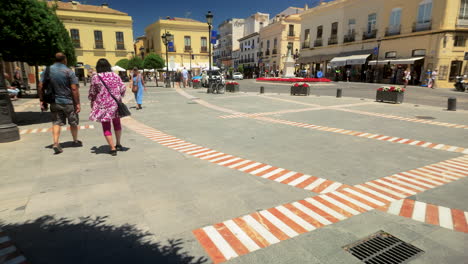 people strolling through a sunny square in ronda, spain, surrounded by historic buildings and vibrant trees, showcasing the town’s lively culture