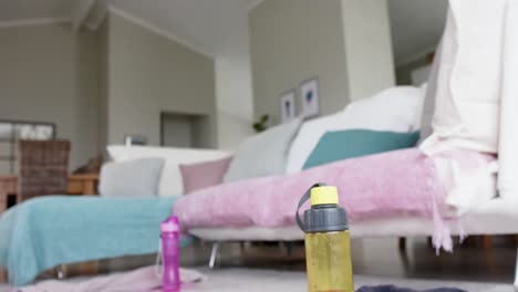 Close-up-of-water-bottles,-towels-and-yoga-mats-on-floor-of-living-room,-slow-motion