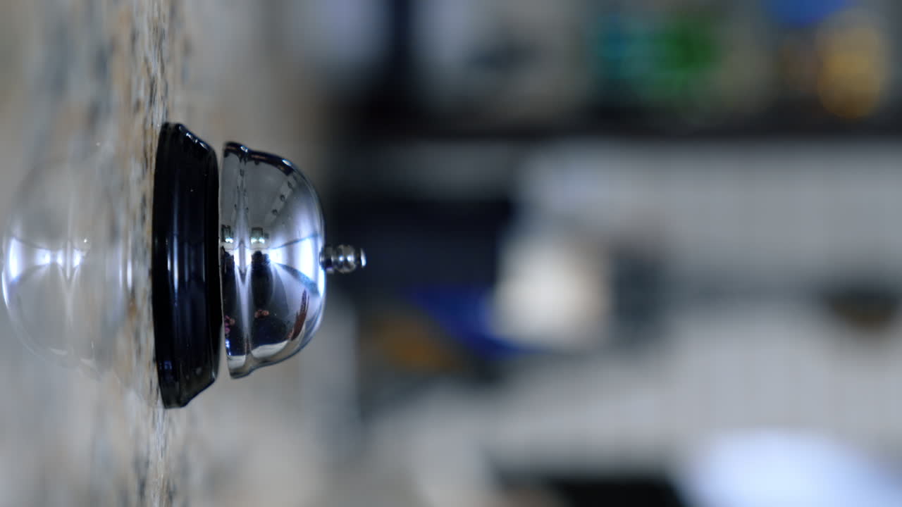 Call bell round on the stand of hotel reception. Female hand presses the bell. Close up. Vertical screen. Blurred backdrop.