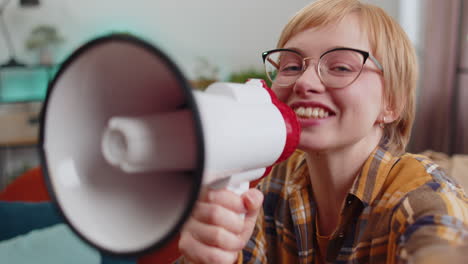 young woman talking with megaphone, proclaiming news, loudly announcing advertisement at home room