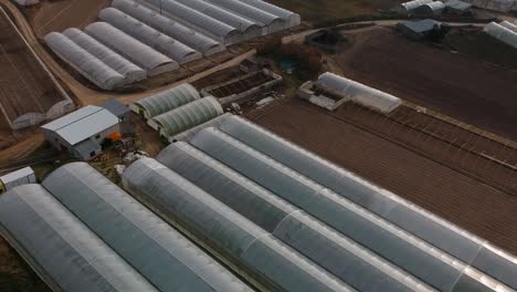 a drone revealing shot of some industrial hothouses, with a river covered with a light mist in the background