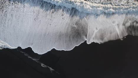 fuertes olas del océano alcanzando la playa de arena negra de islandia al atardecer