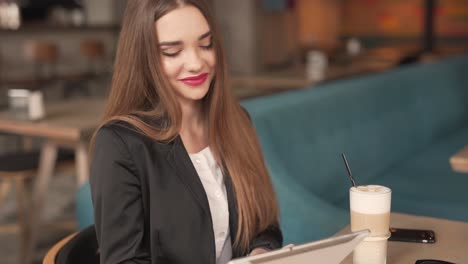 joven caucásica hermosa mujer sentada en el restaurante escribiendo en la tableta y mirando con una sonrisa hacia adelante