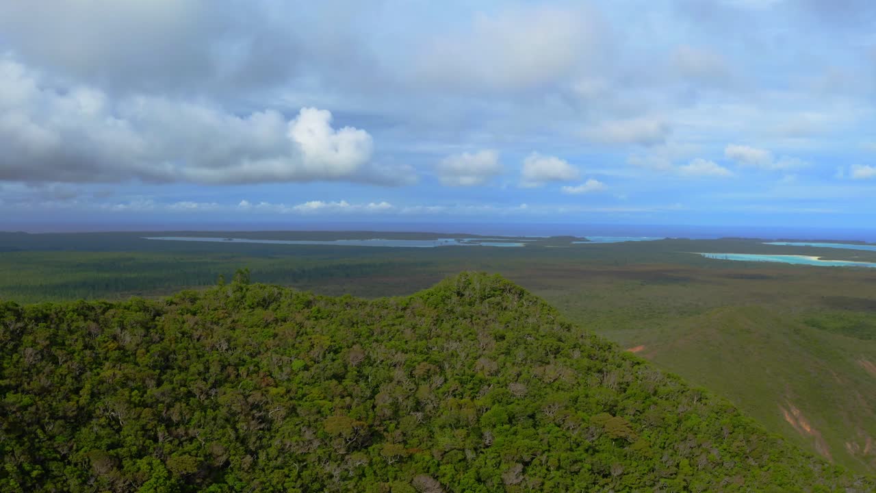 volar sobre una cresta de montaña verde hacia un enorme campo verde con el océano en el horizonte durante un día nublado