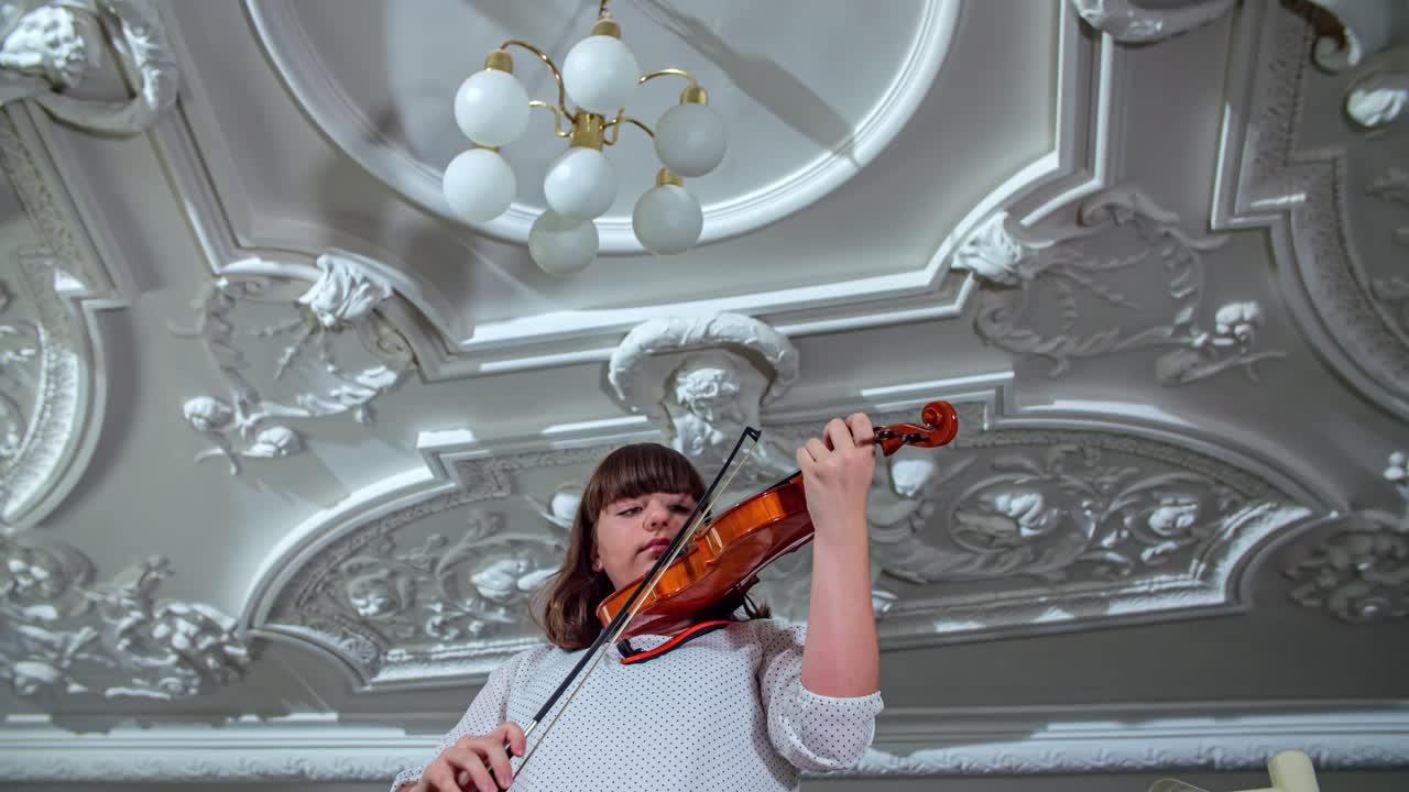 Woman playing violin in old room with stucco and old lamp on the ceiling. Panning shot, low angle