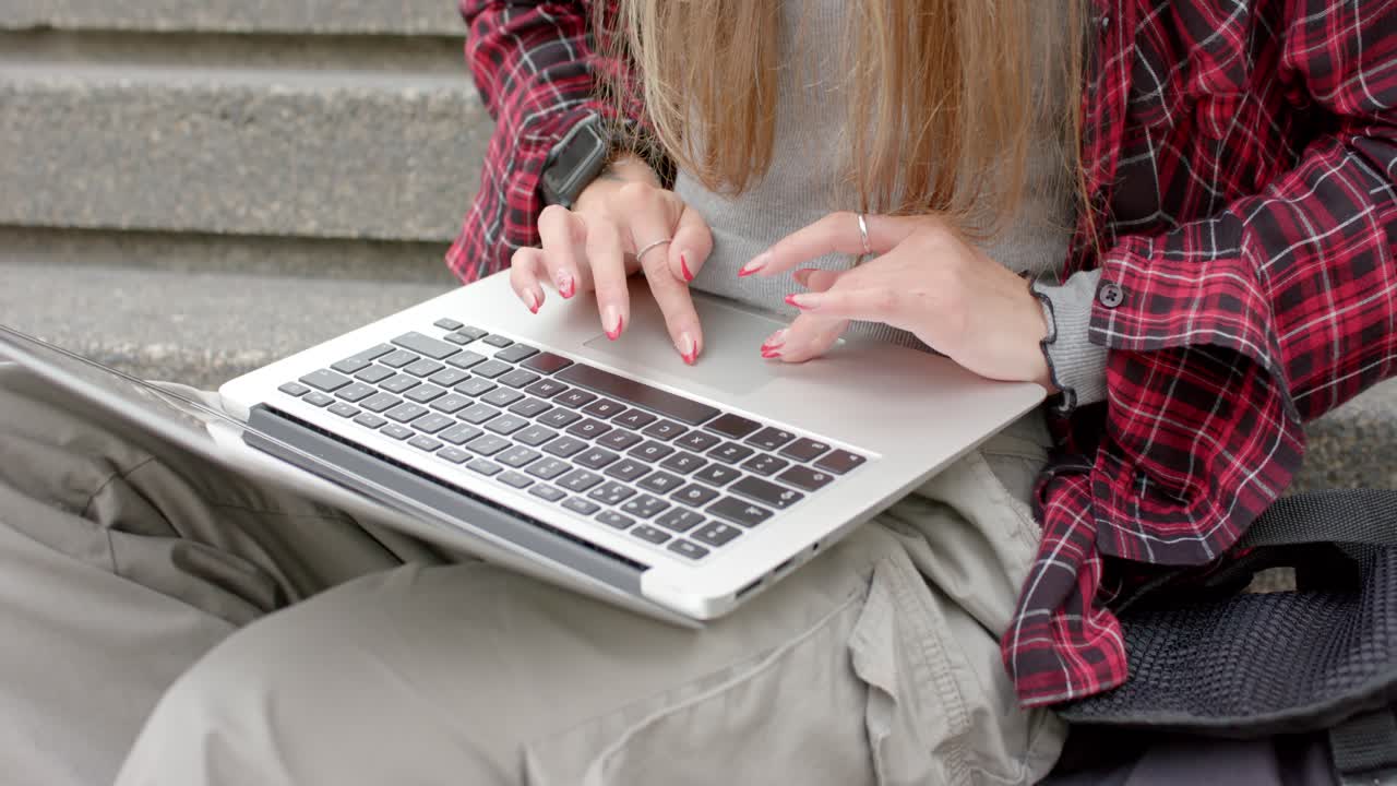 Una donna si sta sistemando sui gradini di cemento, posando un laptop argentato sulle ginocchia e digitando per lavoro da remoto.