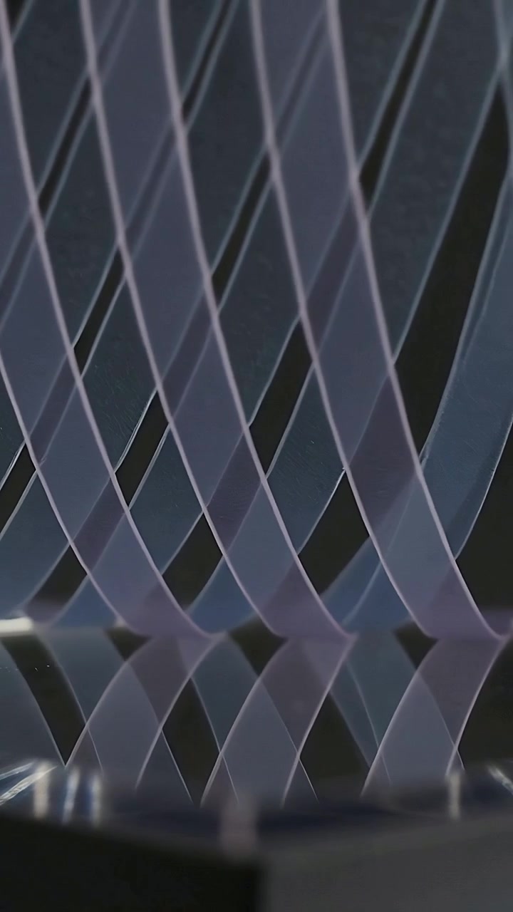 Vertical video: 1st strip lifting waving through clear strips on glass base in studio forming grid