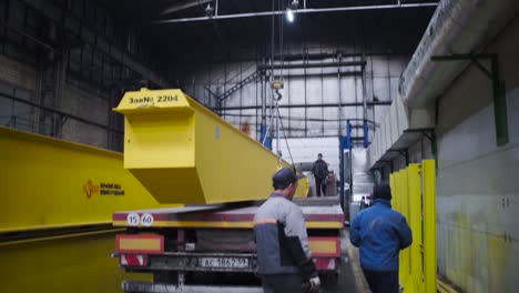 industrial crane lifting a heavy beam on a truck in a factory