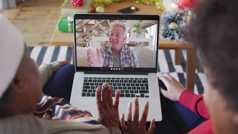 madre y hija afroamericanas usando una computadora portátil para una videollamada de navidad con un hombre en la pantalla