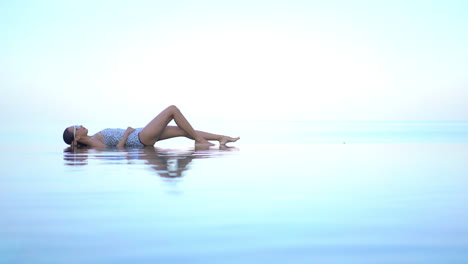 mujer exótica en traje de baño acostada en el borde de la piscina infinita fusionándose con el horizonte del mar tropical, fotograma completo