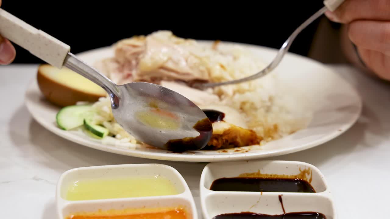 Hand drizzling dark soy sauce over Hainanese chicken rice with roasted and steamed chicken