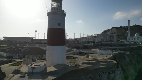 Eine-Atemberaubende-Drohnenaufnahme-Am-Südlichsten-Punkt-Von-Gibraltar,-Die-Um-Einen-Leuchtturm-Kreist-Und-Den-Felsen-Von-Gibraltar-Sowie-Sein-Rugbystadion-Freigibt