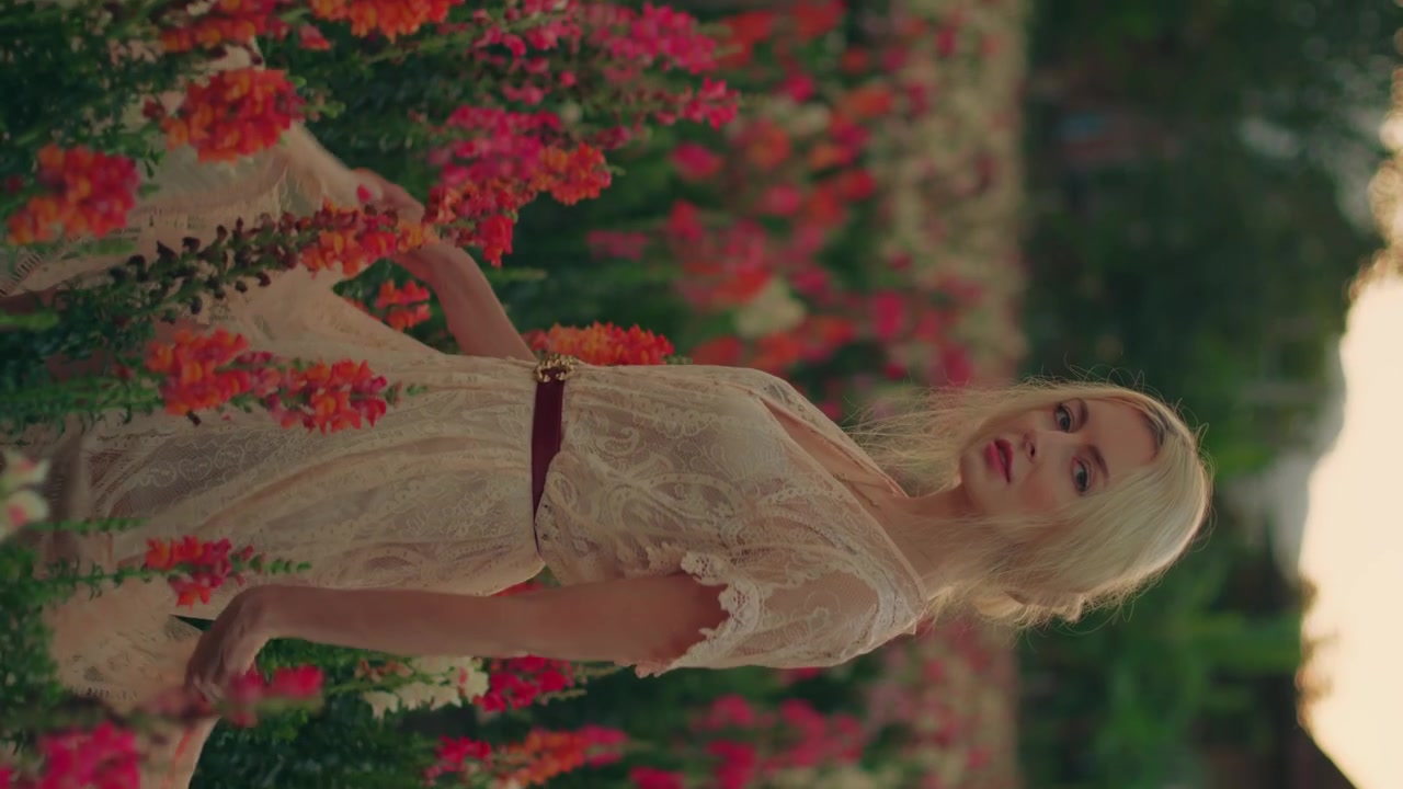 Young Woman in Lace Dress Standing in Flower Field at Sunset