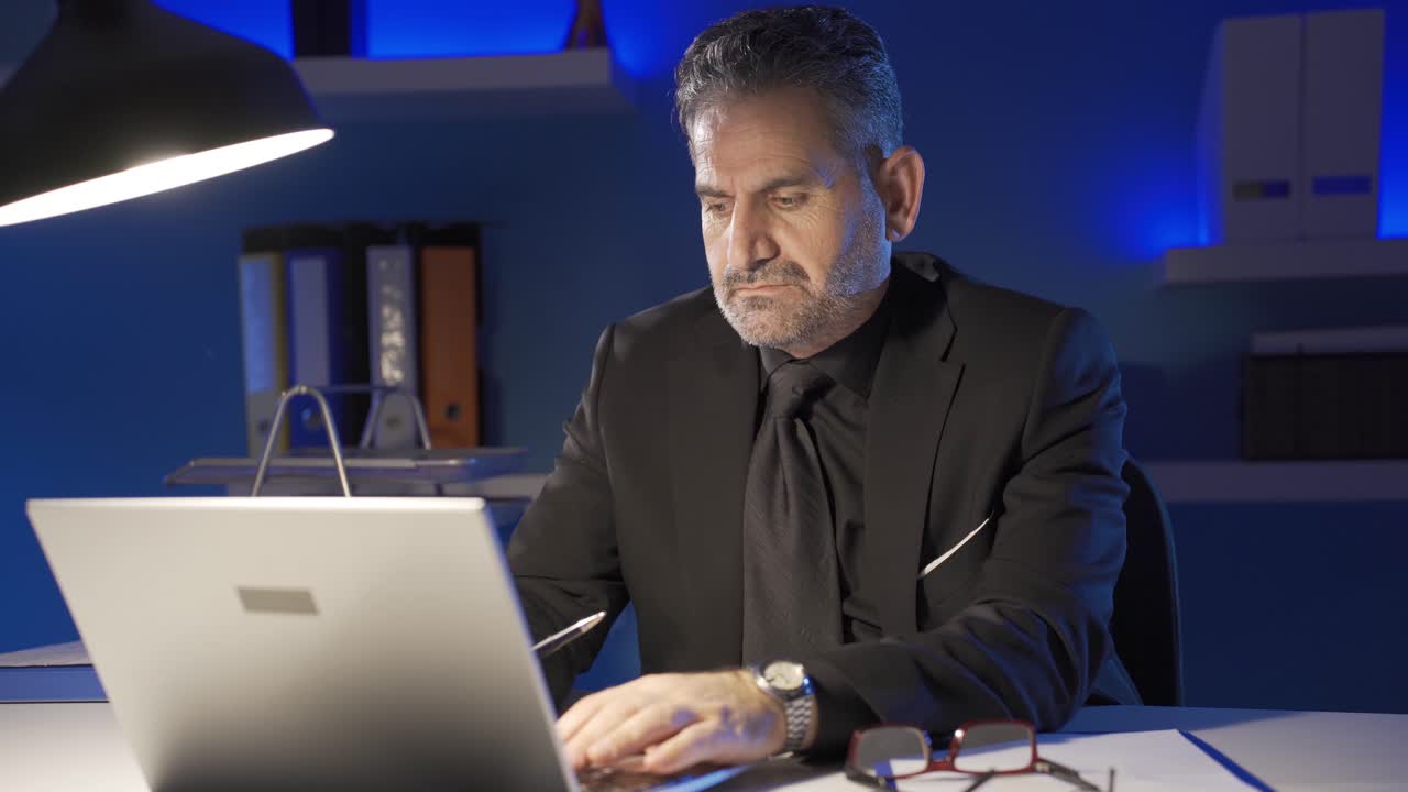 un hombre de negocios maduro, serio y centrado, trabajando tarde en la noche en su computadora portátil en la oficina.