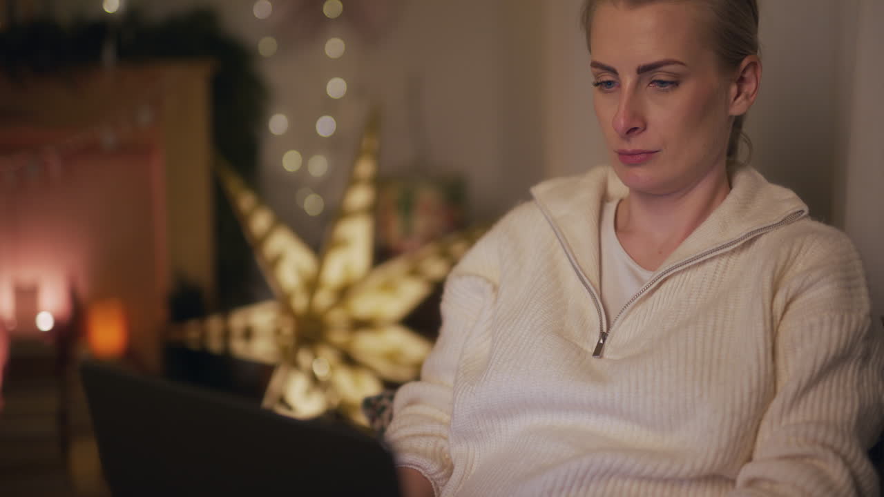 Una donna riflette mentre lavora al laptop di notte, sullo sfondo di decorazioni natalizie