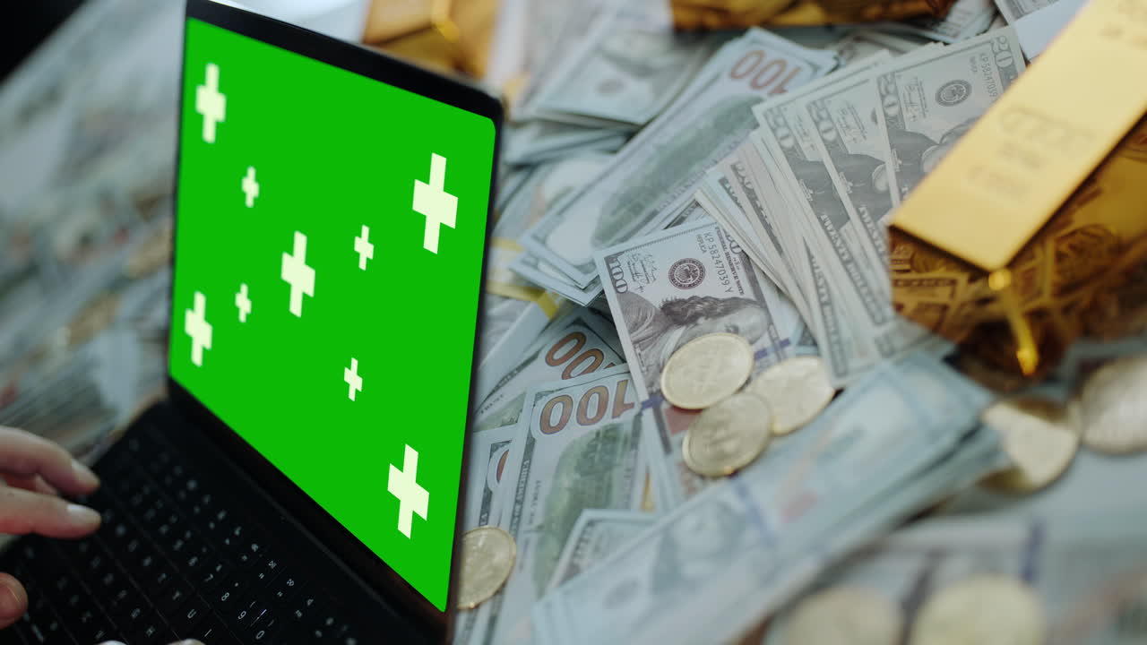 Laptop with Green Screen Display Surrounded by Money and Gold