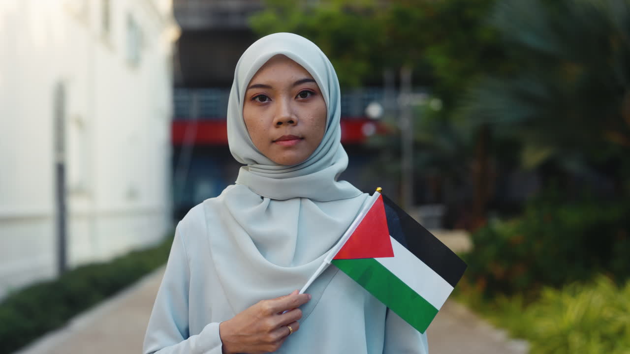 Woman in hijab proudly holds Palestinian flag