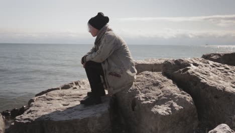 rare view of a tourist sitting on the huge rock while looking at the beautiful calm sea in canada - close-up shot