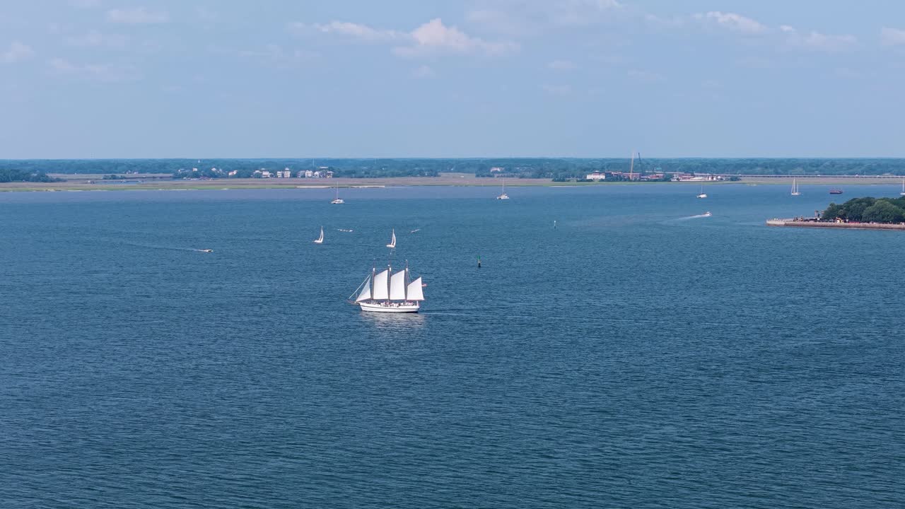 Aerial drone footage of a boat cruising across a blue river near Charleston, with shoreline, wetlands, and distant buildings in view