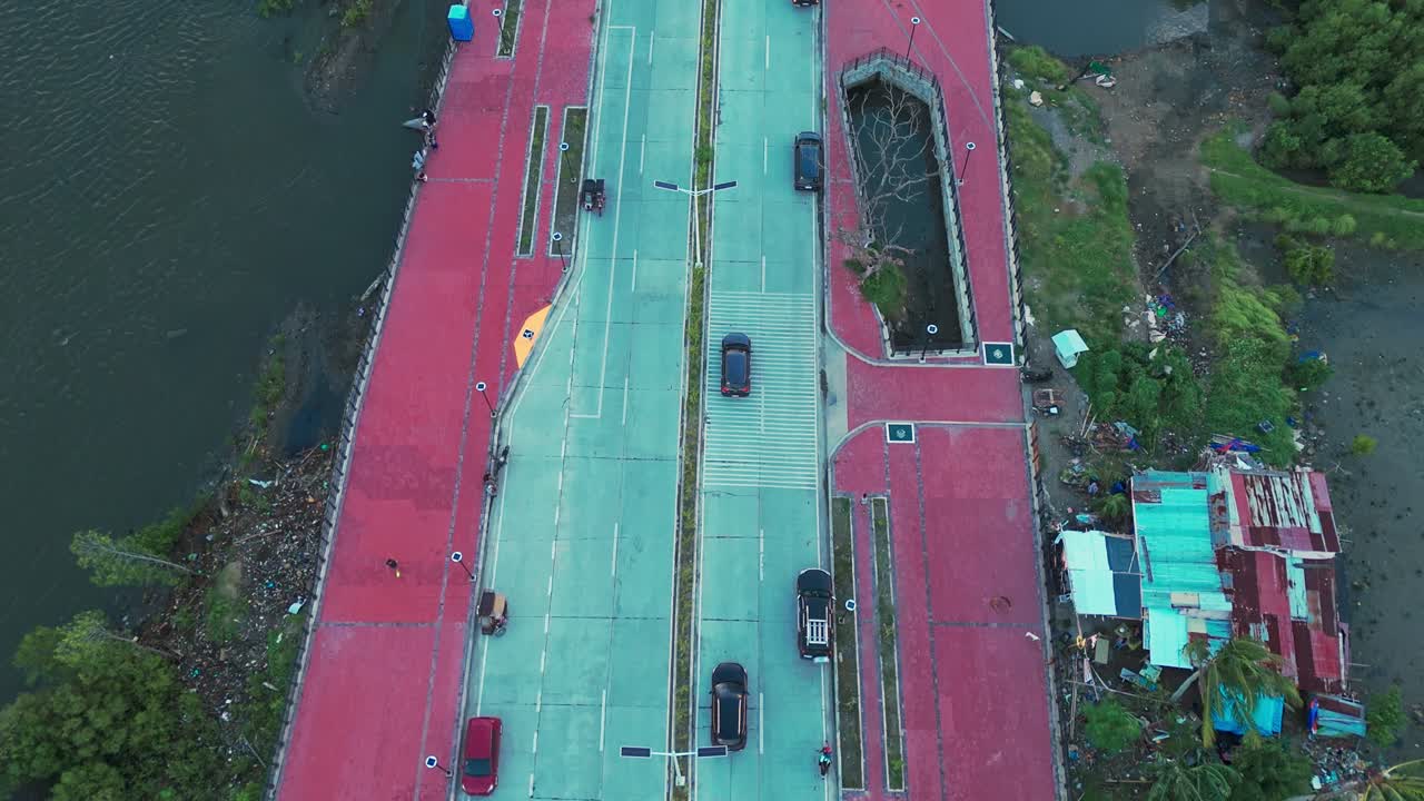 Stunning golden-hour drone view of a riverside road with cars, people, mangroves, and city skyline in the Philippines. Perfect for travel, lifestyle, and urban projects