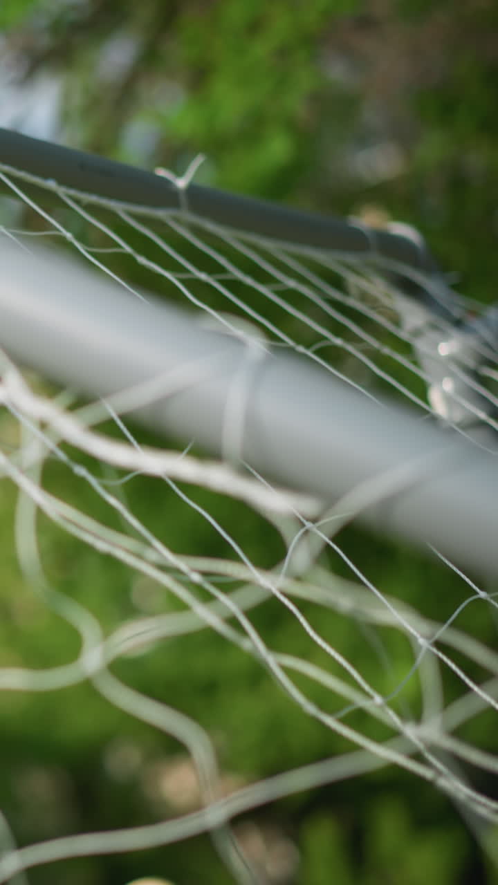 A close-up of a goal post with a ball is shot into the net with precision as the goalkeeper misses, with a blur background of trees