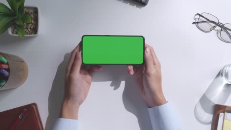 vista de arriba hacia abajo de una computadora portátil con pantalla verde simulada pantalla chromakey en un escritorio de oficina de madera al lado de la libreta con bolígrafos, gafas y un vaso de agua.