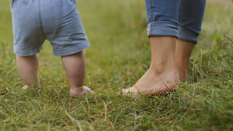 close up of the bare feet of baby and mother taking first steps on the green grass 1