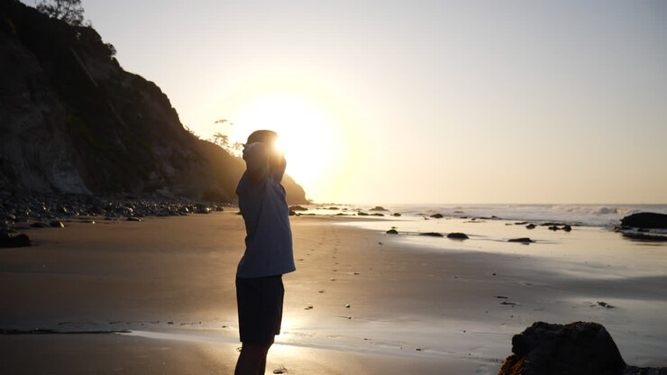 Um homem forte em silhueta respirando e alongando-se após uma corrida e treino matinal na praia ao nascer do sol em Santa Bárbara, Califórnia. CÂMERA LENTA