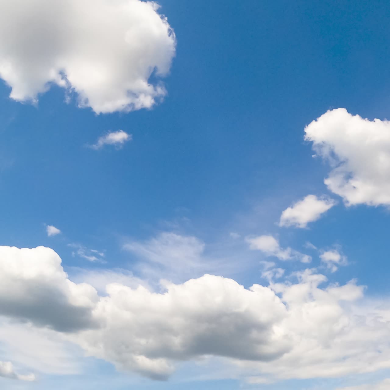 Cumulus and cirrus clouds in the blue sky. White cloudscape in the bright light of the summer sun. Timelapse