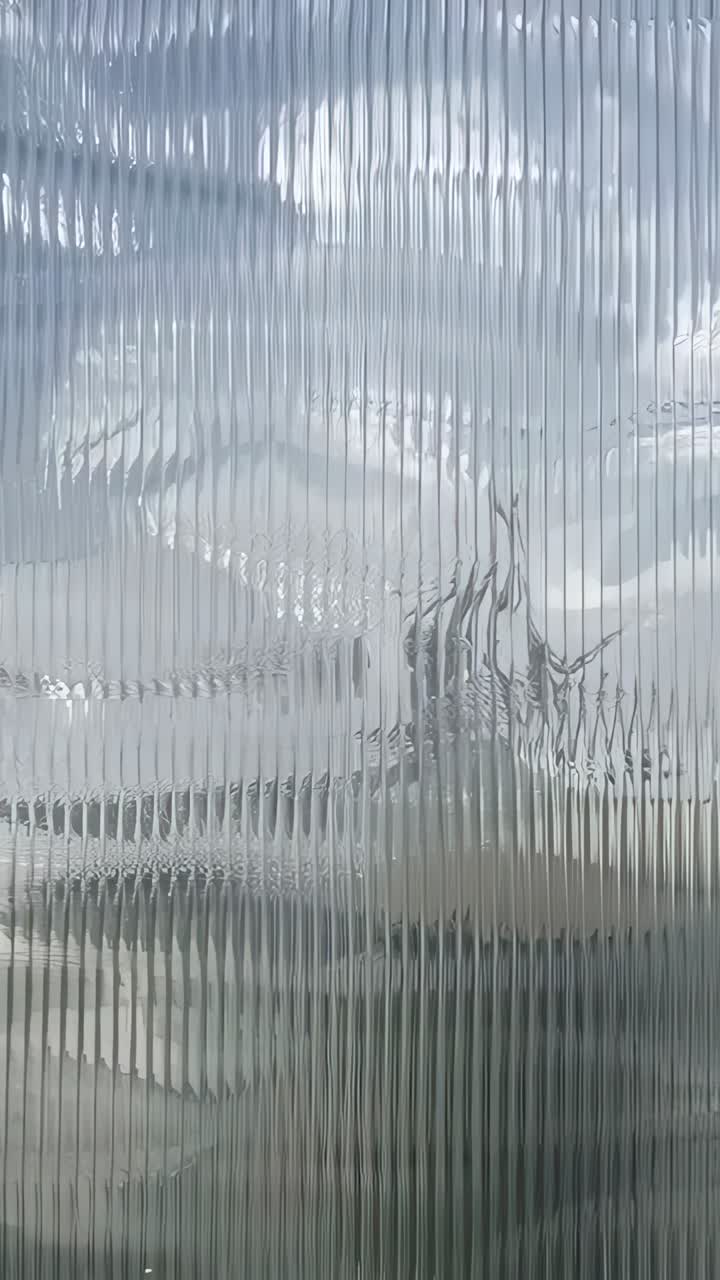 Vertical video: Shifting clouds moving behind ribbed panel on garden wall, showing dark silhouette