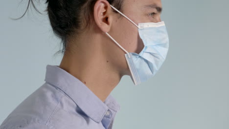 smart young man in shirt placing corona virus face mask covering on and adjusting side profile shot