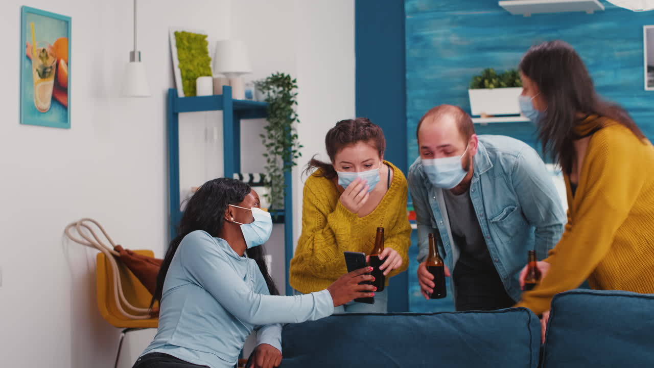 Diverse friends hanging out in living room watching clip on smartphone