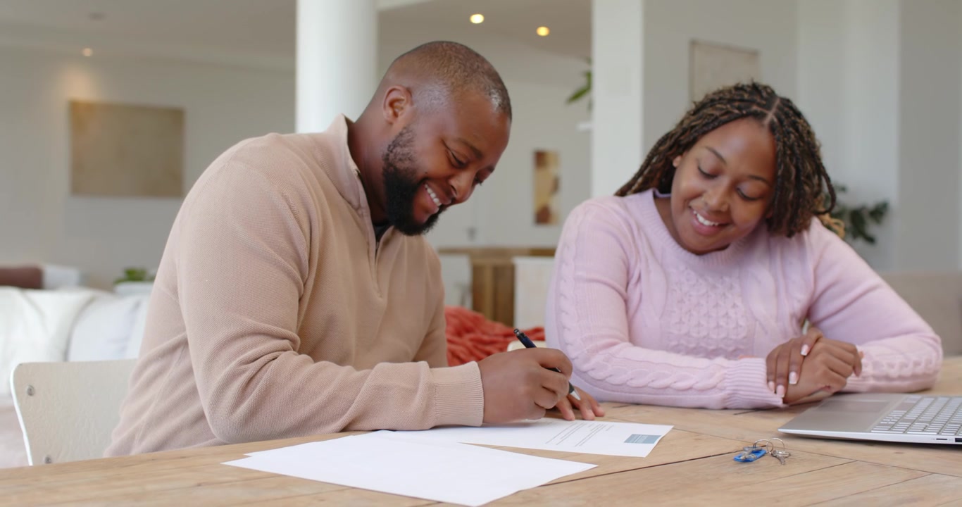 African American couple reviewing papers while man signing with pen to complete forms at home