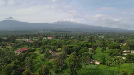 Structures-In-Dense-Foliage-With-Mount-Kilimanjaro-Towering-Behind-During-Misty-Morning-In-Kenya,-Africa