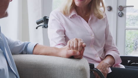 close up de una pareja de mayores con una mujer en silla de ruedas sentada en el salón en casa hablando juntos