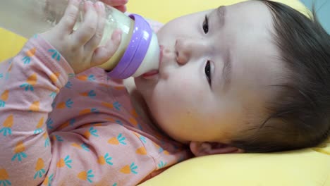 hungry baby drinking formula milk - holding bottle in both hands and looking into the camera