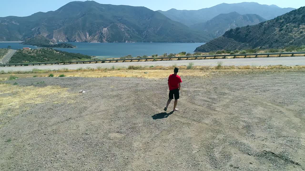 Man walking on a parking lot looking at mountains and a lake