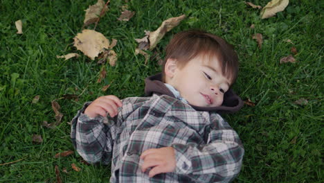 Happy-asian-kid-lies-on-the-grass-and-autumn-leaves