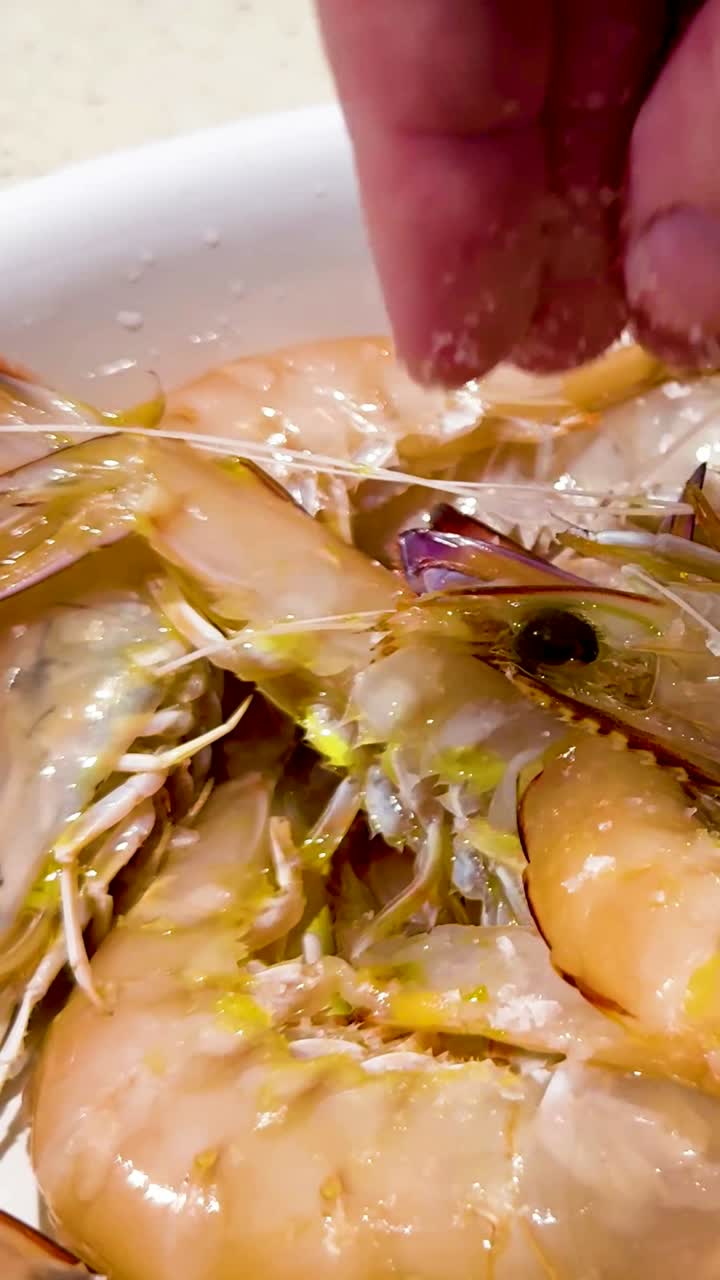 손은 접시에 있는 신선한 새우 위에 소금을 뿌립니다.