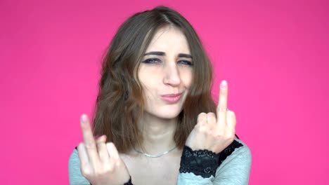 young woman showing middle finger gesture while looking at the camera over pink background.