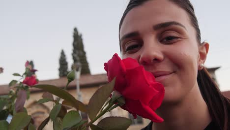 modelo femenino con rosa roja cerca de la cara mirando a la cámara y sonriendo