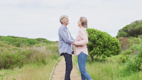 smiling senior caucasian couple embracing and walking on path outdoors