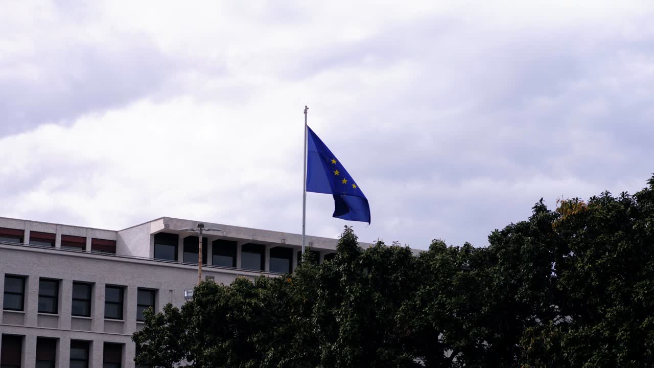 flag of Europe with the circle of twelve stars flutters in the cloudy sky