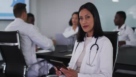 mixed race female doctor sitting in meeting room using tablet smiling