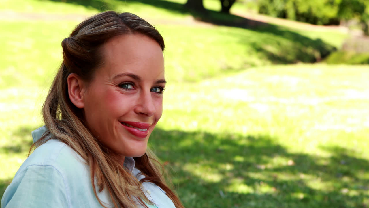 Smuk blondine smiler til kameraet i en park