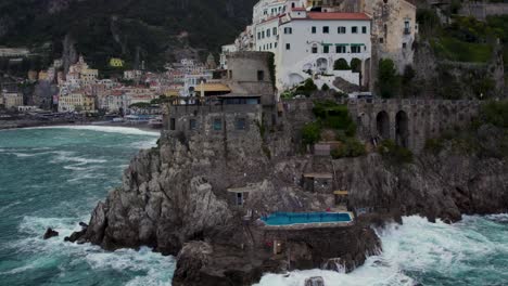 Piscina-De-Lujo-En-El-Acantilado-En-La-Costa-De-Amalfi,-Vista-Aérea-De-Las-Olas-Golpeando-En-La-Orilla