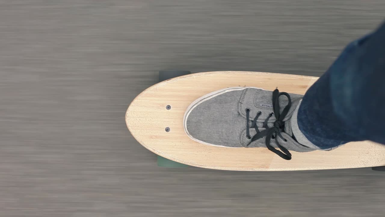 Scatto verticale, primo piano ravvicinato in soggettiva dall'alto di uno skater che usa lo skateboard o un cruiser board sull'asfalto